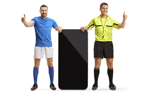 Full length portrait of a referee and a football player standing next to a big mobile phone and gesturing thumbs up isolated on white background