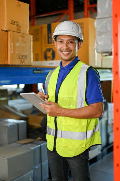 istock Handsome Asian warehouse worker smiling, looking at camera while working in warehouse. 1442364293
