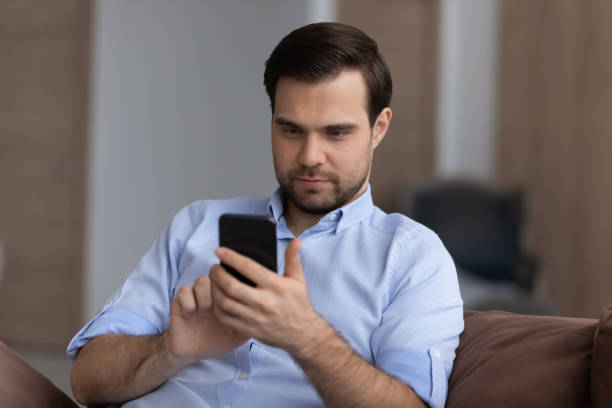 istock Focused guy spend time on couch browse web on phone 1442364787