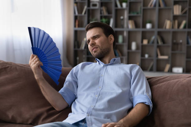 istock Exhausted young male recline on sofa hold fan wave himself 1442364818