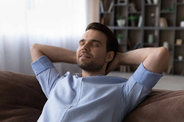 istock Peaceful young casual guy relax on couch hands over head 1442364834