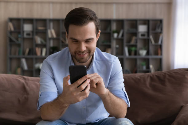 istock Smiling casual millennial male sit on couch chat on cellphone 1442364836