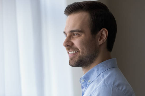 Smiling businessman stand by window look at distance create plans