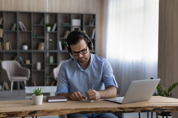 istock Focused young man student wear headphones handwriting before pc screen 1442364913