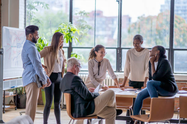 Casual Business Meeting A small group of business professionals casually meet in a downtown office as they discuss new strategies and goals for the company.  They are each dressed professionally and are casually sitting around and on a boardroom table. happy workers stock pictures, royalty-free photos & images