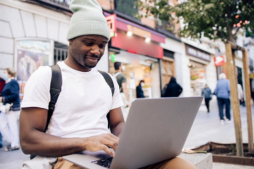 Portrait of a young African American tourist exploring Madrid and using laptop on the street.