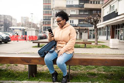 Portrait of a beautiful African American girl taking a break in the city and using smartphone
