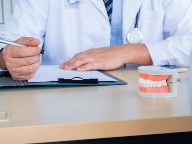 istock Close up a tooth model on desk while dentist make writing with a patient file document on clipboard in medical clinic office with copy space. Oral dental check up concept. 1442372265
