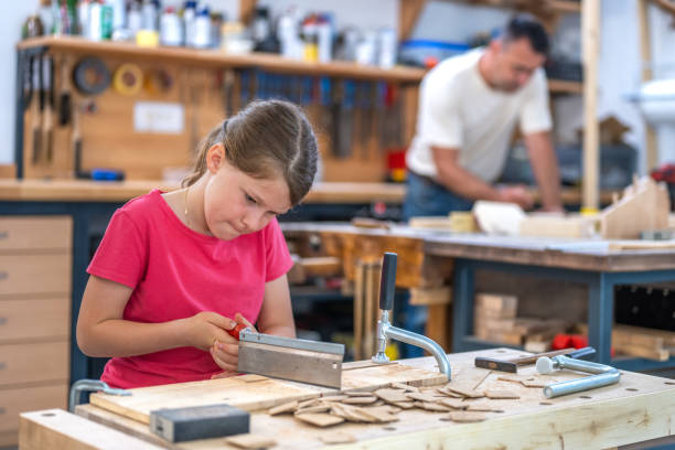 istock Girl cutting wooden plank with handsaw in carpentry workshop classroom 1442372421