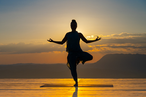 Silhouette of woman practice yoga on top of the mountain against a sunset - Concept of meditation stretching and relaxation