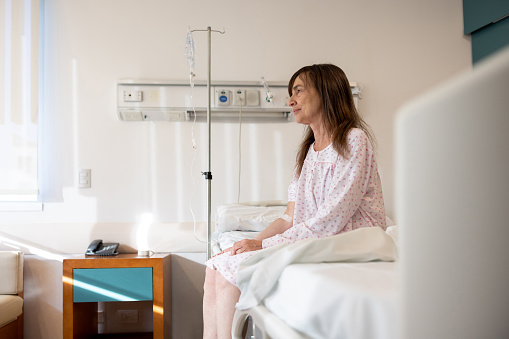 Sick woman sitting on the edge of her bed at the hospital - healthcare and medicine concepts
