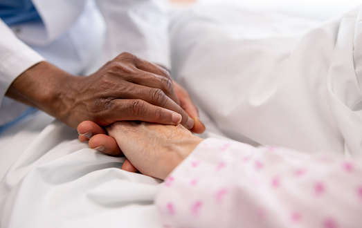 Primer plano de un médico sosteniendo la mano de una mujer enferma en la cama del hospital photo
