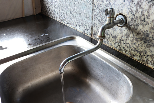 Photo of water faucet in the sink, for washing dishes and washing hands, this household appliance is usually in a house, apartment or hotel