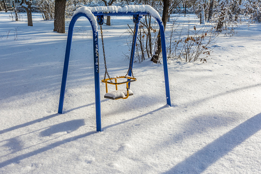 An old children's swing covered with snow in a city park. Winter cityscape