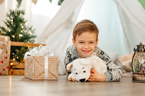 A little boy lying in a children's wigwam decorated for Christmas with gifts