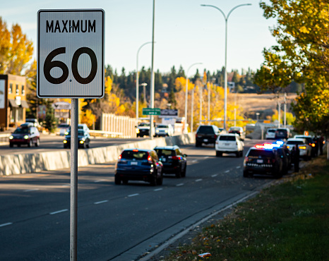 'Maximum 60' speed limit signage with police cars with emergency lights activated-- blurred in the background.