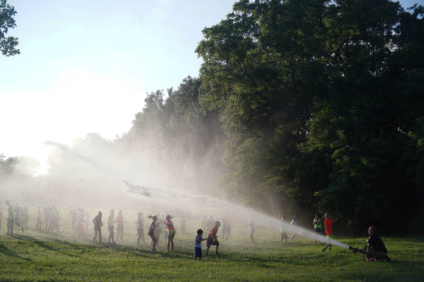 пожарная служба шланга воды охлаждает детей, играющих в парке в канзас-сити, сша - kansas city missouri стоковые фото и изображения