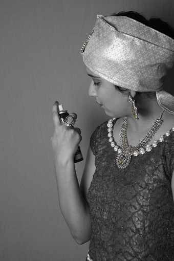 A grayscale shot of a beautiful Asian female in traditional dress and jewelry using perfume