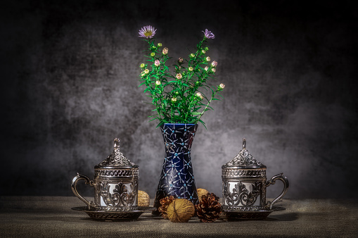 A closeup shot of antique silver cups and sauces and a vase with flowers on the table