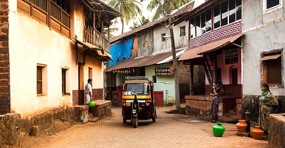 Gokarna, India – January 29, 2014: The urban view of the yellow rickshaw and local people with jugs of water in a street, Gokarna, India