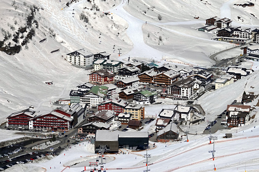 chalets in alpine village covered with snow at the end of a white rural road and mountain background