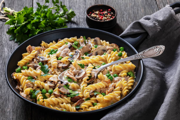tuna mushroom green pea fusilli with creamy cheese sauce in pan on dark wood table, landscape view from above