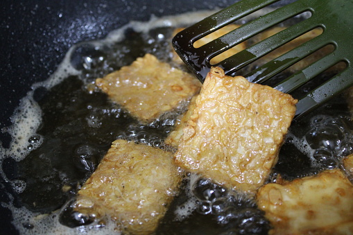Woman frying tempeh a traditional Indonesian food made from fermented soybeans