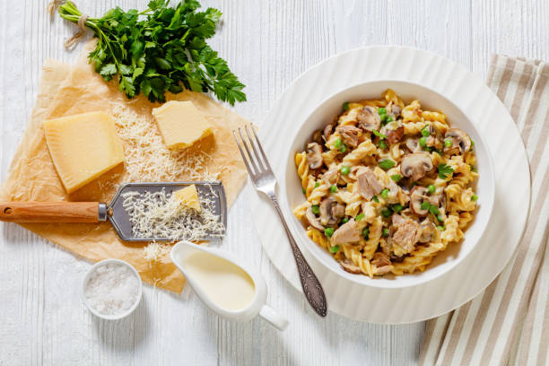 tuna mushroom green pea fusilli casserole with creamy cheese sauce in white bowl on white wood table, flat lay