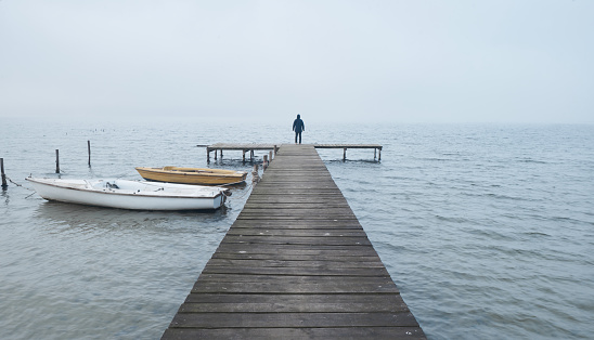 Man standing on a wooden jetty or pier at a lake at foggy morning.