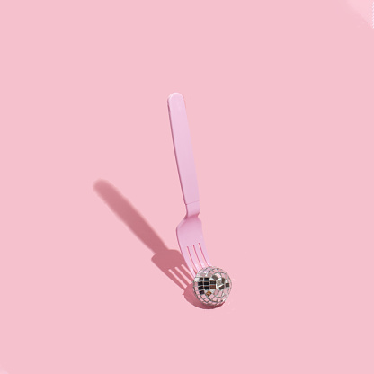 Christmas creative layout with disco ball christmas decoration and pink fork on pastel pink background. New Year aesthetic food concept. Minimal surreal idea.