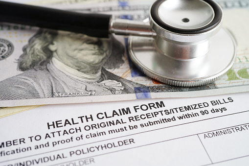 Health claim form with stethoscope and US dollar banknotes, insurance accident medical concept.