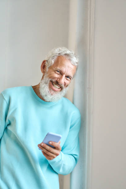 istock Happy senior bearded hipster man using mobile phone standing at white wall. 1442437986