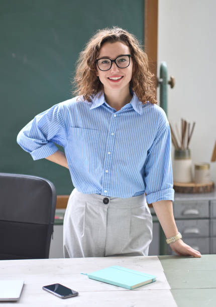 giovane insegnante felice allenatore in piedi alla scrivania nell'ufficio della classe. ritratto - professor teacher female blackboard foto e immagini stock
