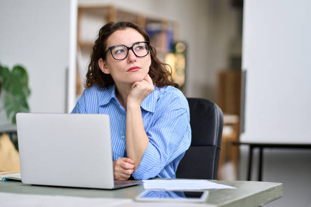 Thoughtful serious professional woman using laptop, looking away thinking.