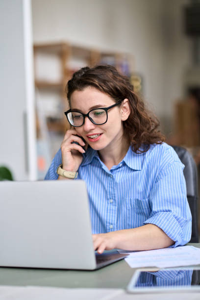 istock Young woman talking on the phone using laptop working online. Vertical 1442442016
