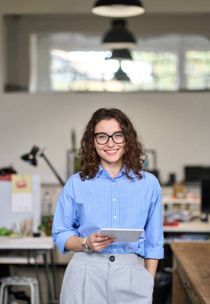 istock Young happy female manager holding tablet standing in office, vertical portrait. 1442442021
