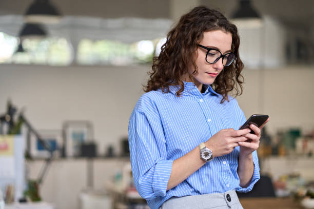 istock Young business woman holding mobile phone standing in office using cell. 1442442037