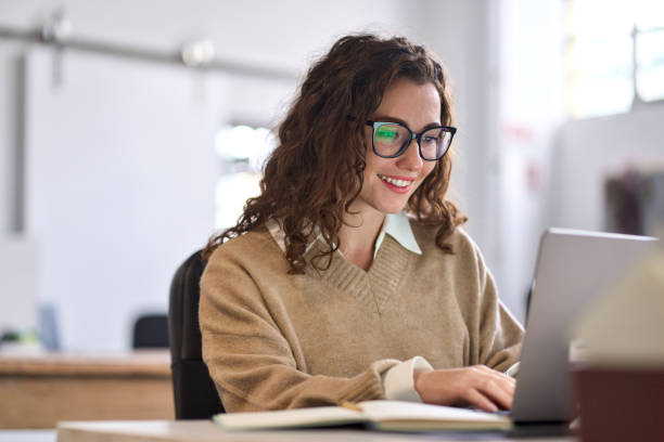 jovem empregada ou estudante feliz sentado na mesa usando laptop. - typing busy business women - fotografias e filmes do acervo