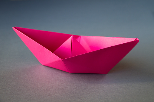 Pink paper boat origami isolated on a blank grey background.