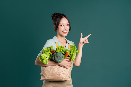 Asian girl portrait holding a bag of vegetables on a green background
