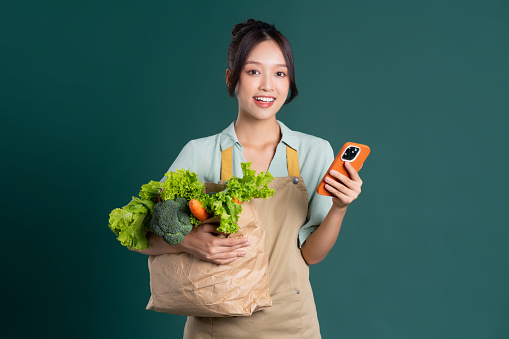 Asian girl portrait holding a bag of vegetables on a green background