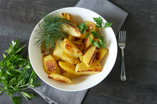 istock Baked potato slices with herbs in a white plate, top view. 1442443946