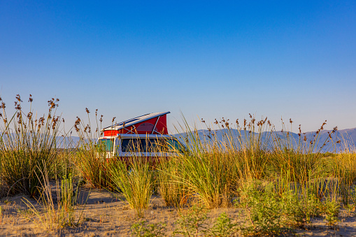 Red motor home moving amidst grass in sandy beach against sky during summer