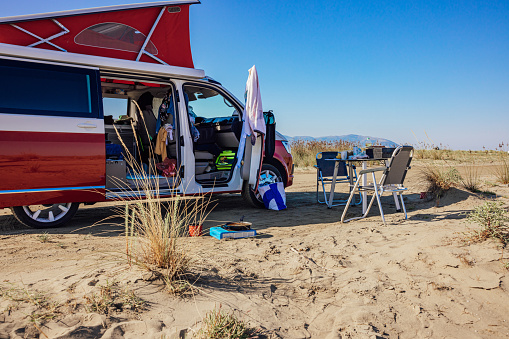 Empty table and chairs outside campervan on sandy beach against clear sky during sunny day