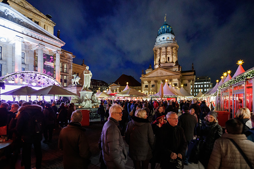 Berlin, Germany - December 10, 2018: Gendarmenmarkt square, traditional Christmas market in front of illuminated German church Deutscher Dom and concert hall Konzerthaus with people in the street visiting stalls in the evening