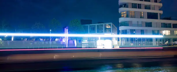 Lighttrails of a boat passing at night throug a city with some buildings in the background