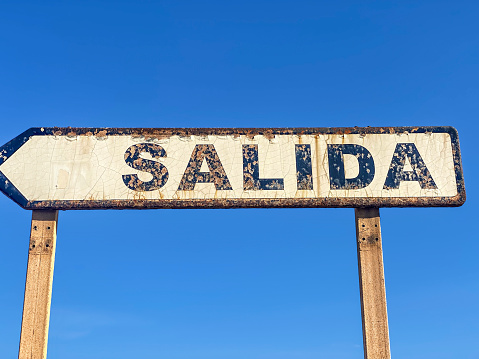 Low angle view of rusty exit sign against clear sign showing the Spanish word SALIDA