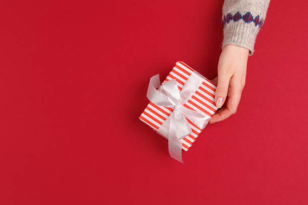 istock Female hands with christmas gift on red background, top view, copy space 1442455646