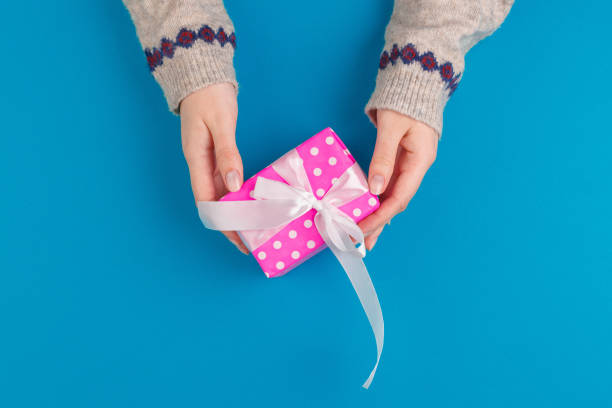 istock Small gift box in female hands on blue background, view from above 1442456037