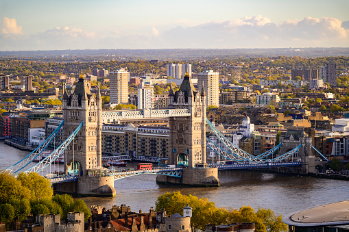 Panoramic aerial view of the skyline of London, England, with a ship crossing under the Tower Bridge during a beautiful sunset